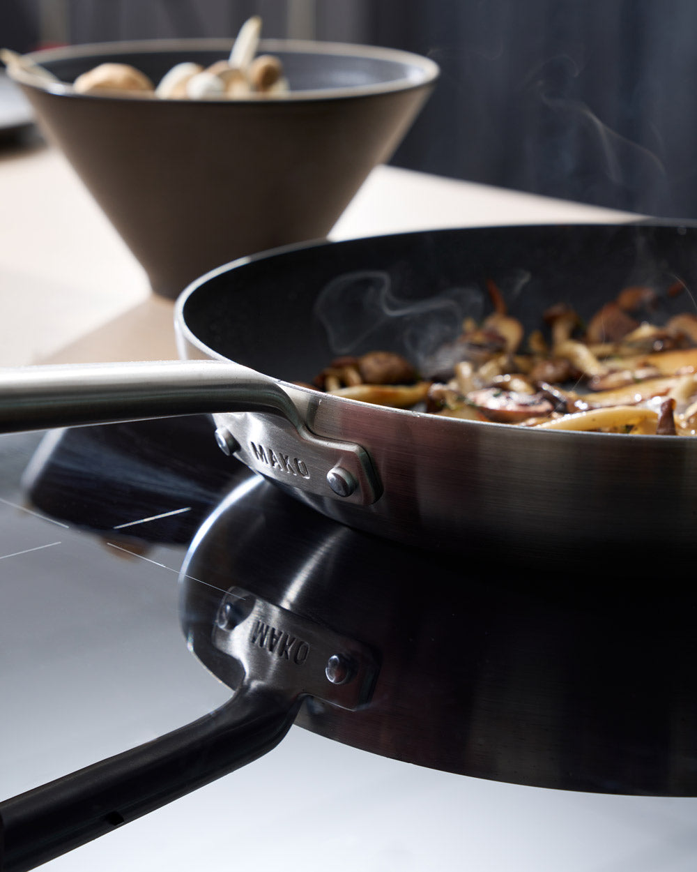 Non-stick frying pan on stovetop with cooked vegetables, bowl of mushrooms in background
