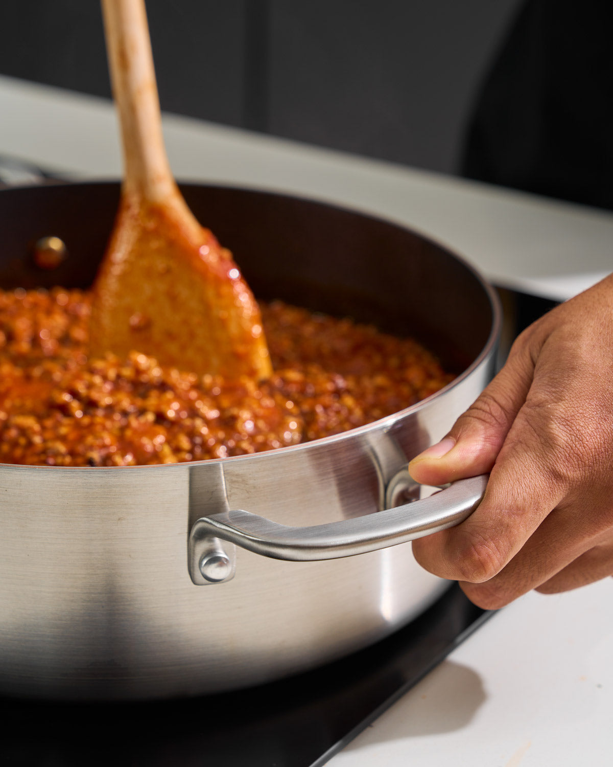 Stainless steel frying pan with sauce being stirred on stovetop, close-up kitchen scene