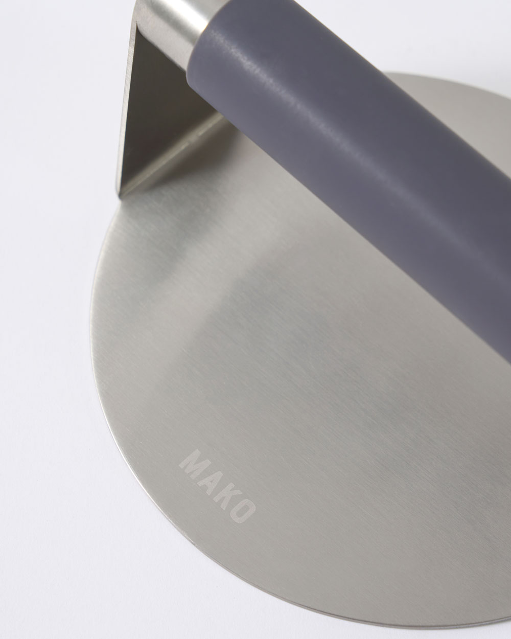 Stainless steel press with ergonomic handle and MAKO logo, close-up kitchen tool