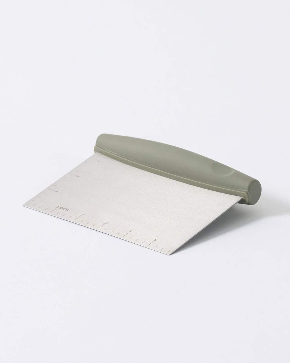 Stainless steel kitchen scraper with grey handle and measurement markings on white background.