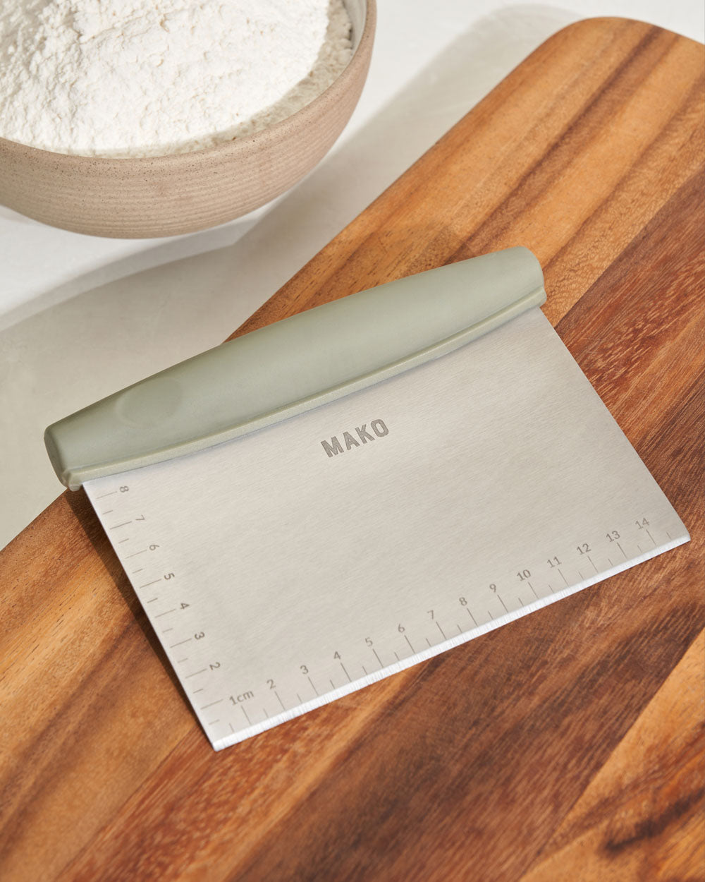 Stainless steel kitchen bench scraper with measurement markings and ergonomic handle on wooden board
