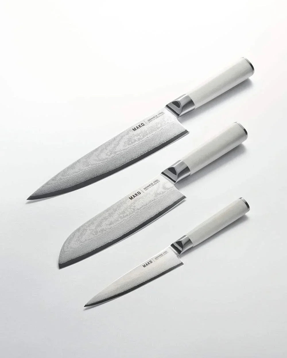 Set of three Mako Japanese steel kitchen knives with white handles on white background