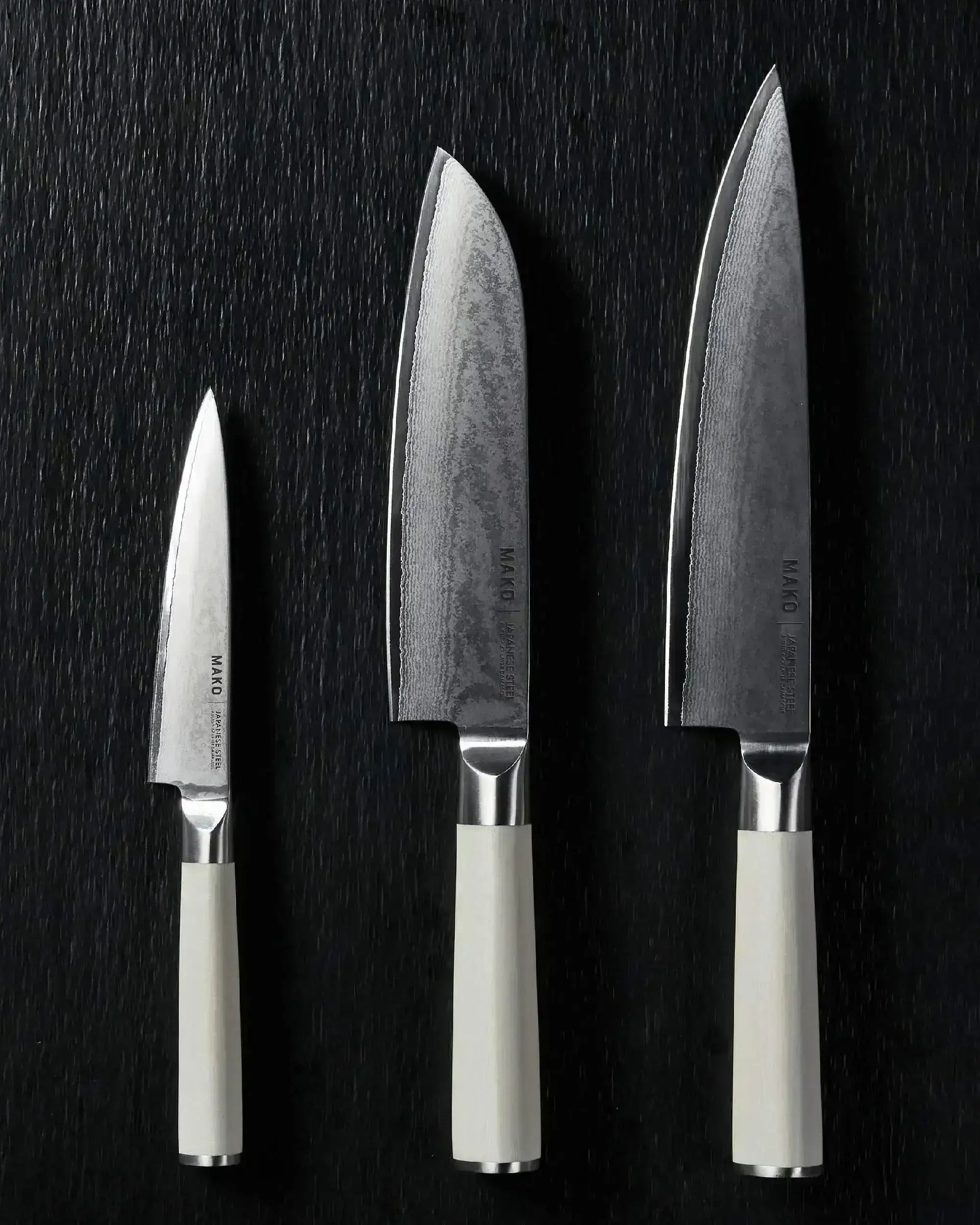 Three Japanese steel kitchen knives with cream handles on a black textured background.