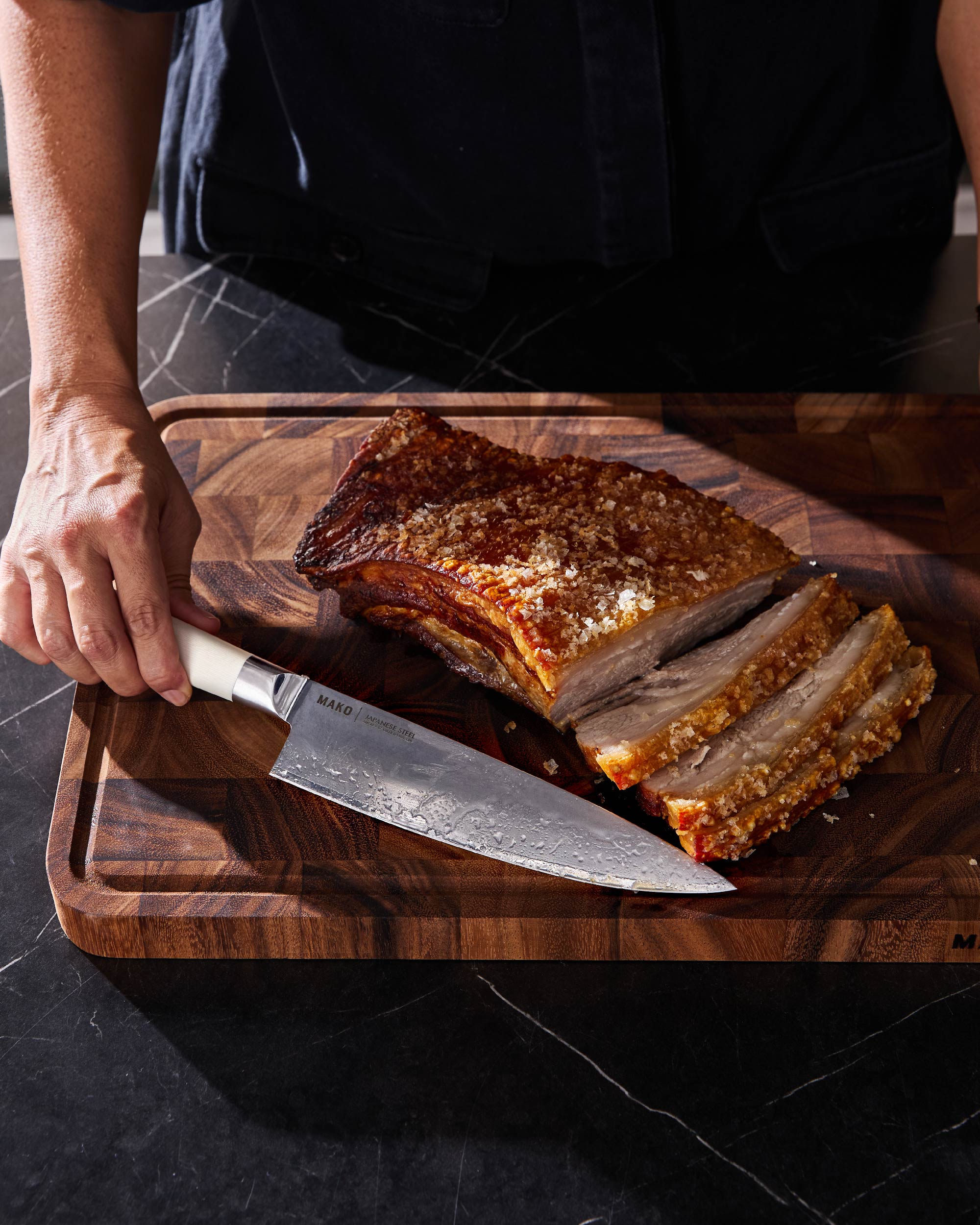 Japanese steel kitchen knife slicing crispy pork on wooden cutting board