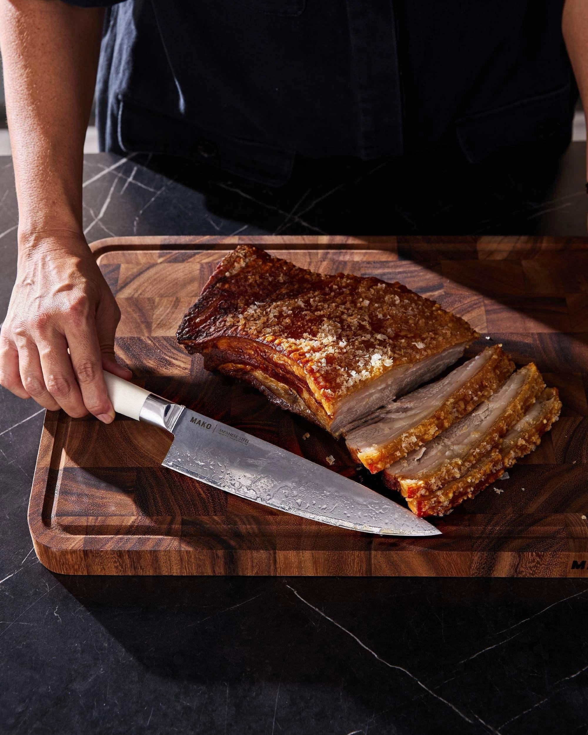 Japanese steel chef knife with cream handle slicing roasted pork on wooden cutting board
