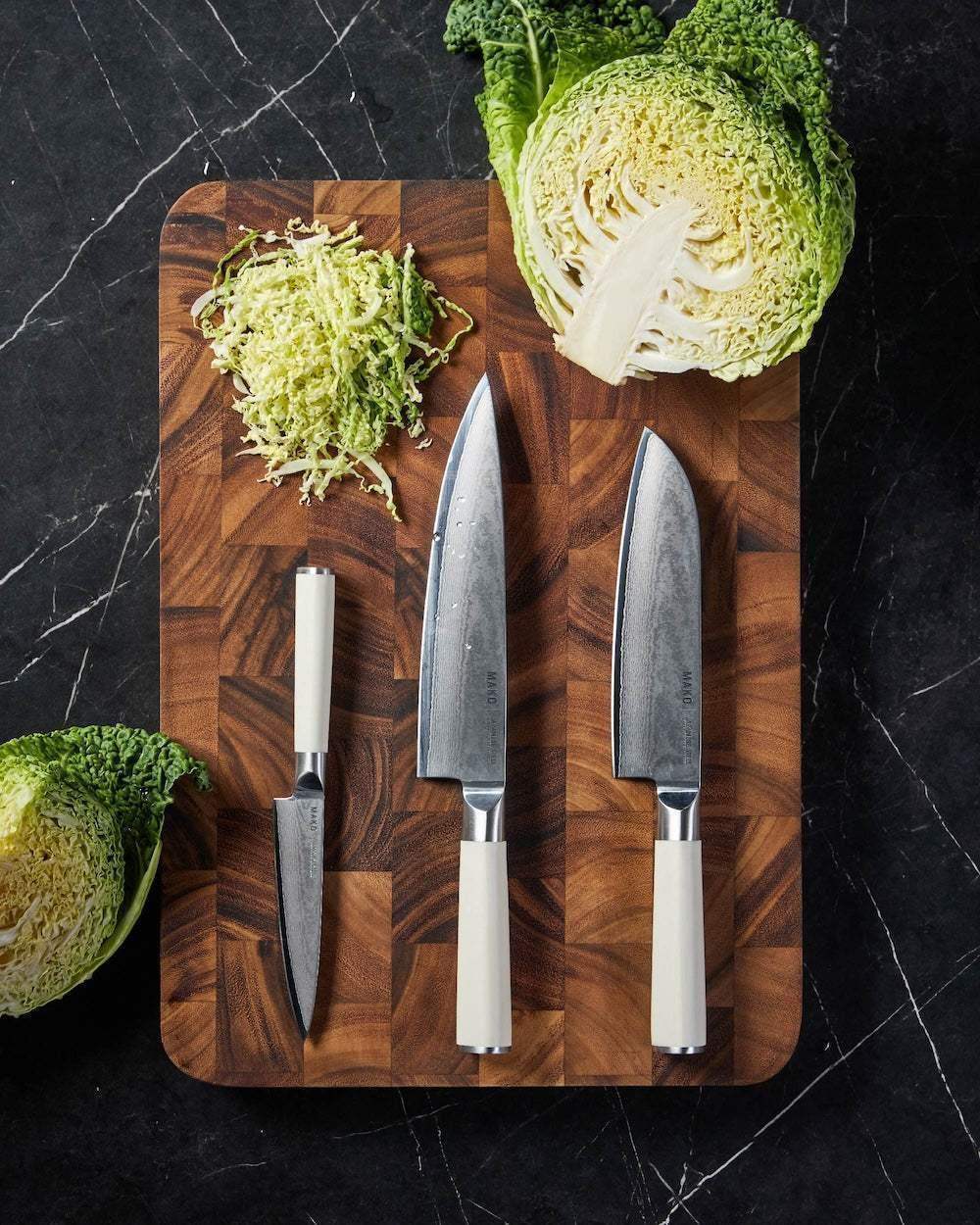 Japanese steel knife set with cream handles on wooden cutting board, cabbage sliced