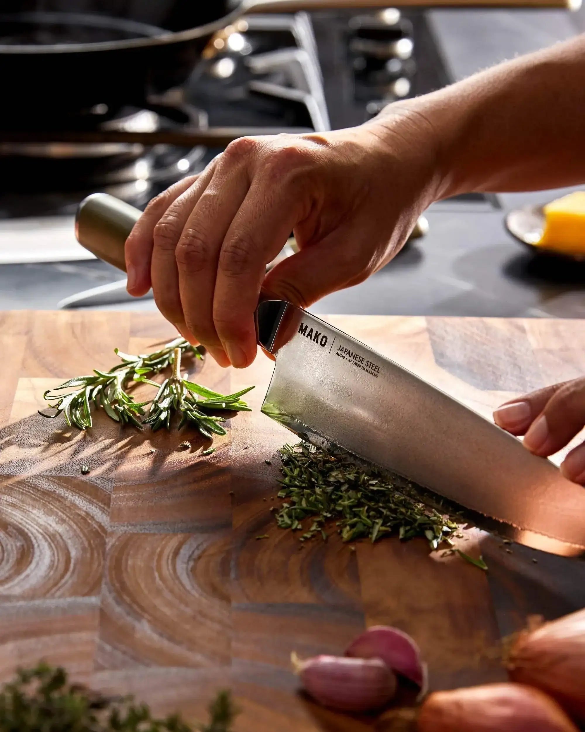 Hand chopping rosemary on wooden cutting board with Marion Grasby's Mako Japanese steel knife