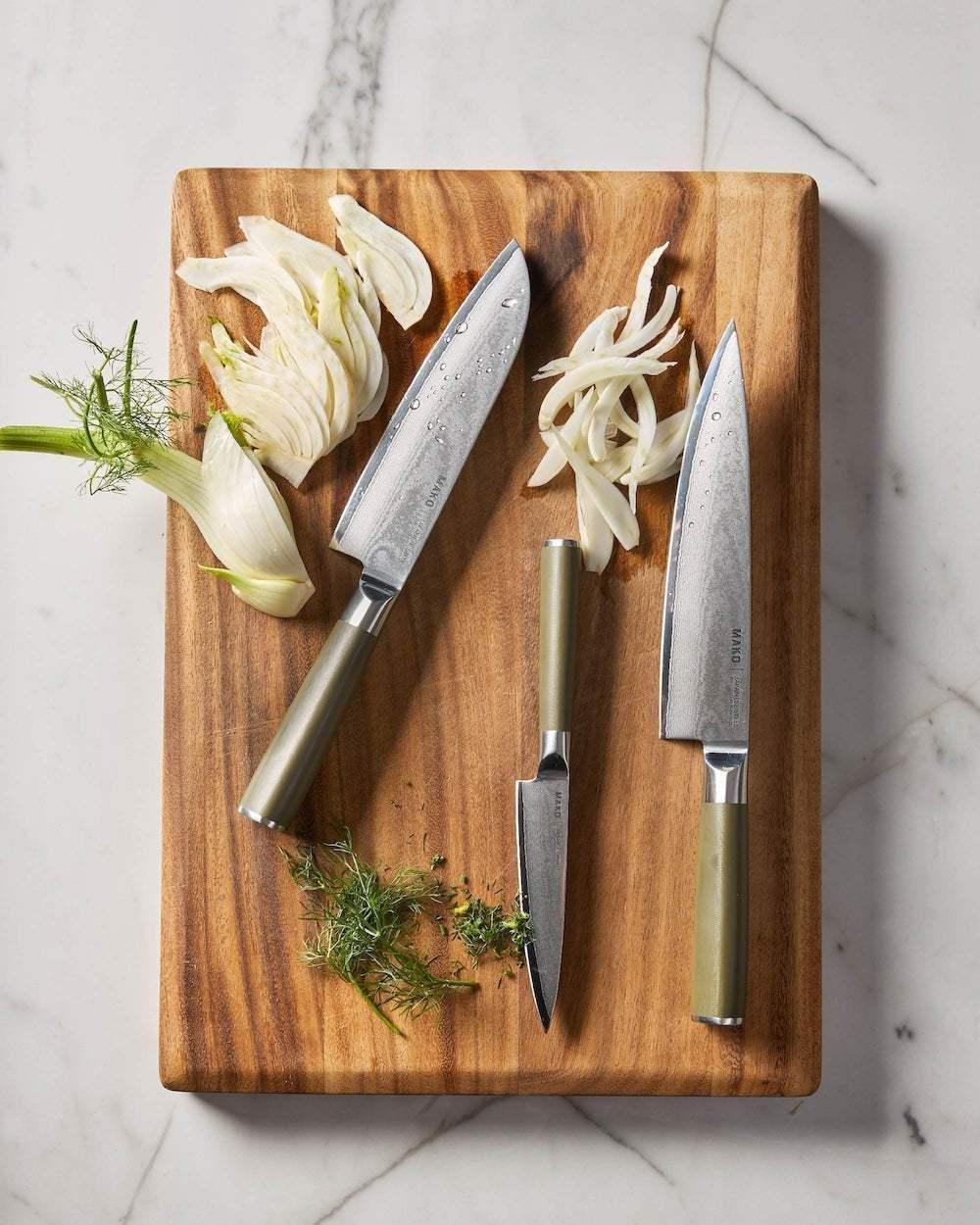 Japanese steel knife set with olive green handles on wood cutting board with sliced fennel