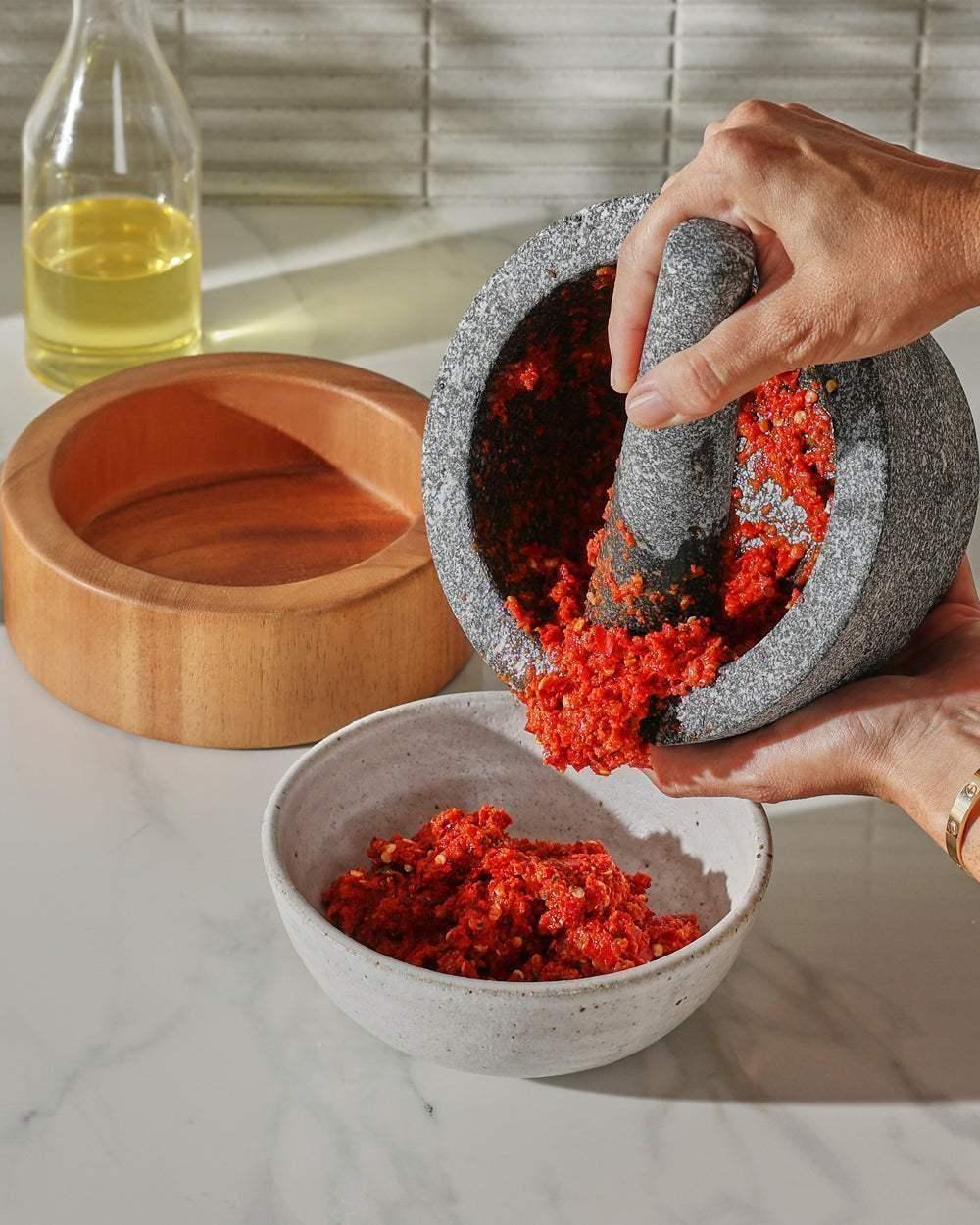 Granite mortar and pestle grinding fresh red chili paste, marble kitchen counter background