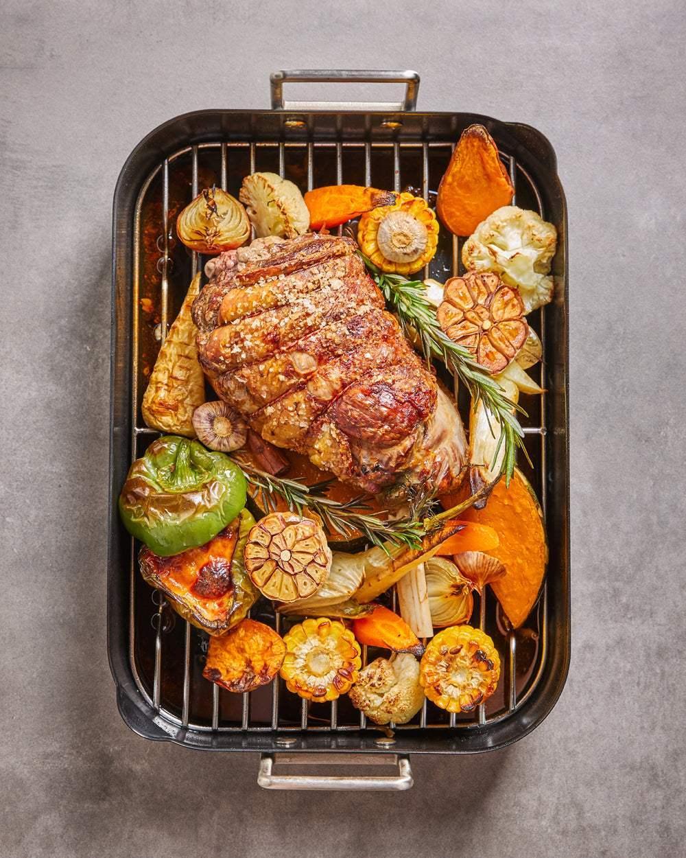 Roasted meat with salt and assorted grilled vegetables in a black non-stick roasting pan on a gray surface