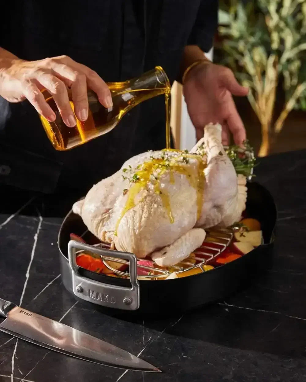 Pouring oil over raw chicken in an oval non-stick roaster with vegetables
