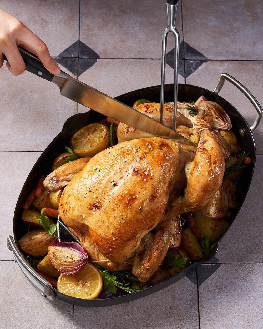 Roast chicken with vegetables and lemon in non-stick oval roasting pan, being carved