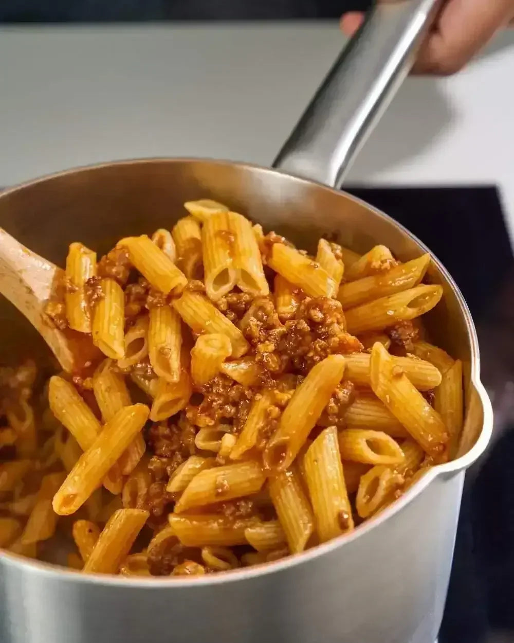 Stainless steel saucepan cooking penne pasta with meat sauce on stovetop