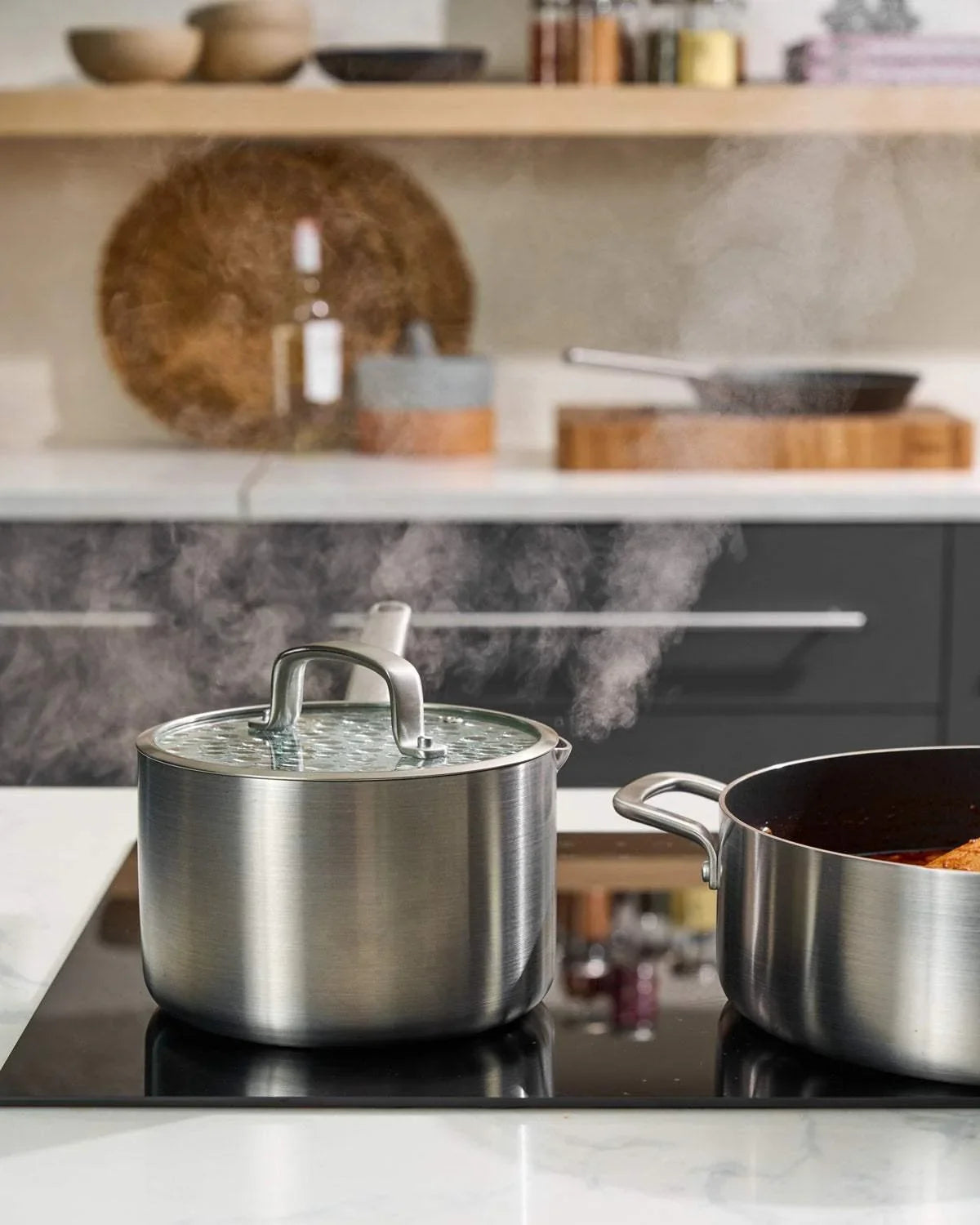 Stainless steel saucepan with glass lid and steam on modern kitchen stovetop