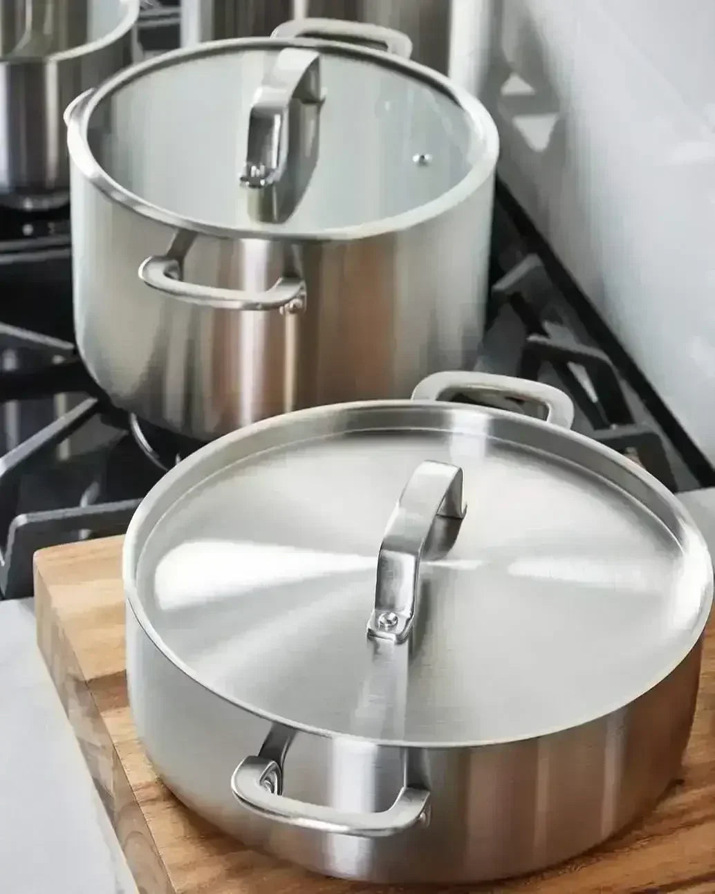 Stainless steel saucepans with lids on stovetop and wooden board, modern kitchen setting