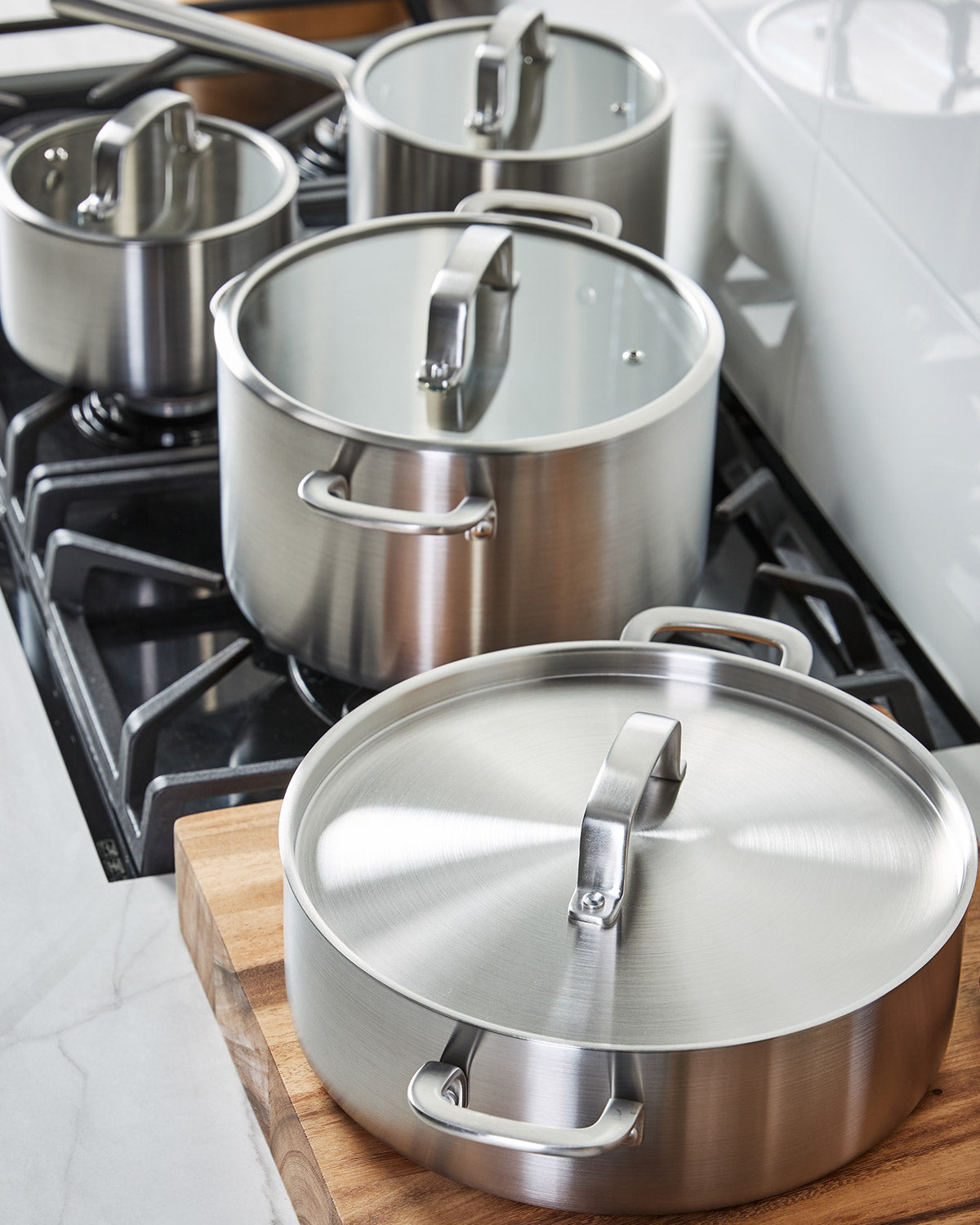 Stainless steel saucepans with lids on stovetop and wooden board, modern kitchen setting