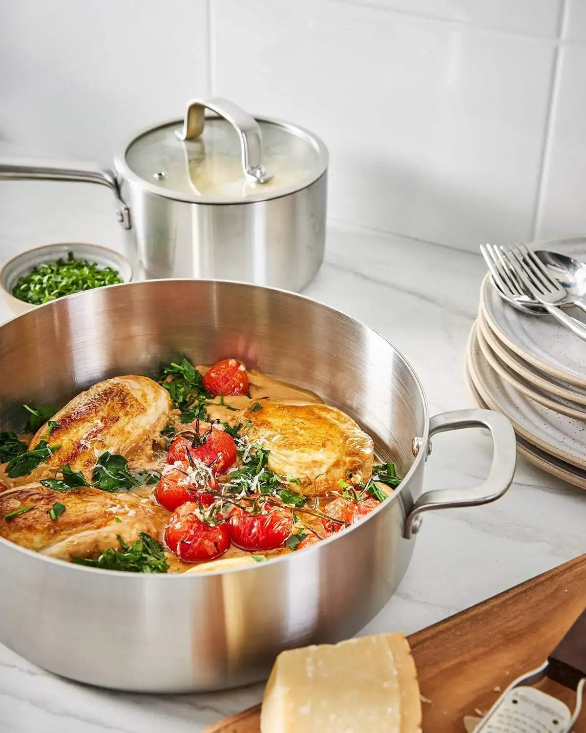 Mako stainless steel saucepan cooking chicken with tomatoes and herbs on marble countertop