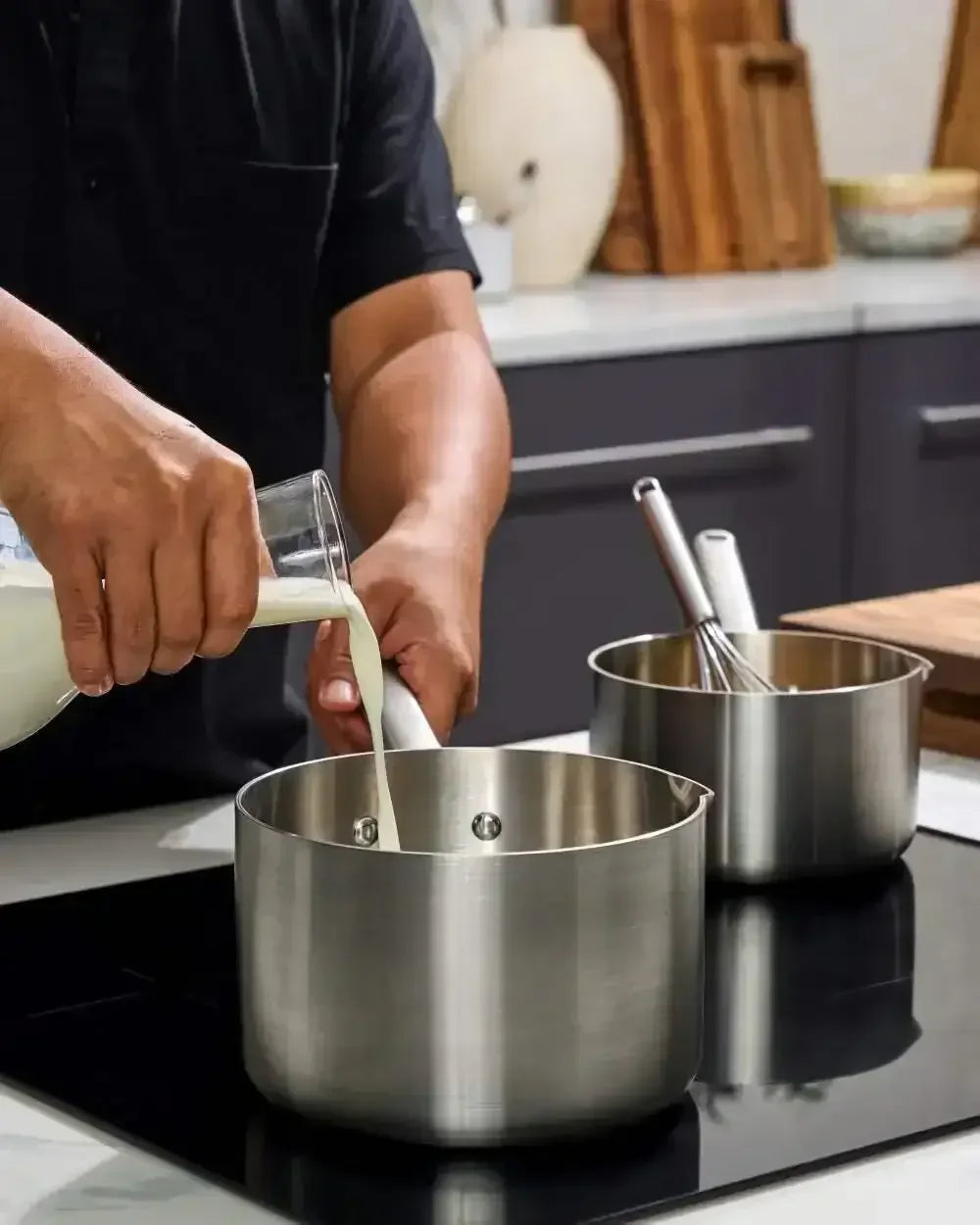 Person pouring milk into stainless steel saucepan on induction cooktop in modern kitchen