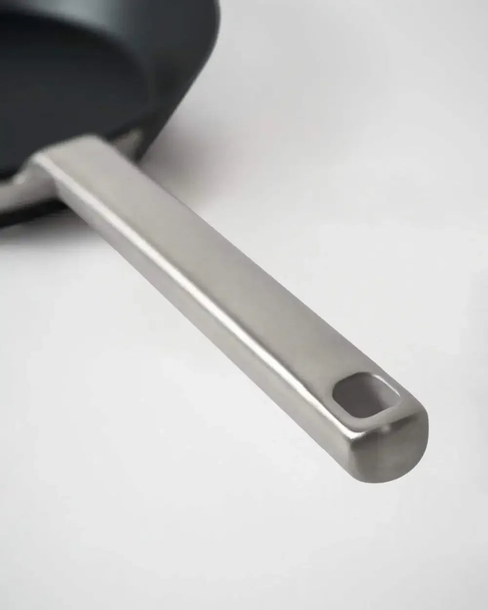 Close-up of a black steel skillet with a stainless steel handle on a light background