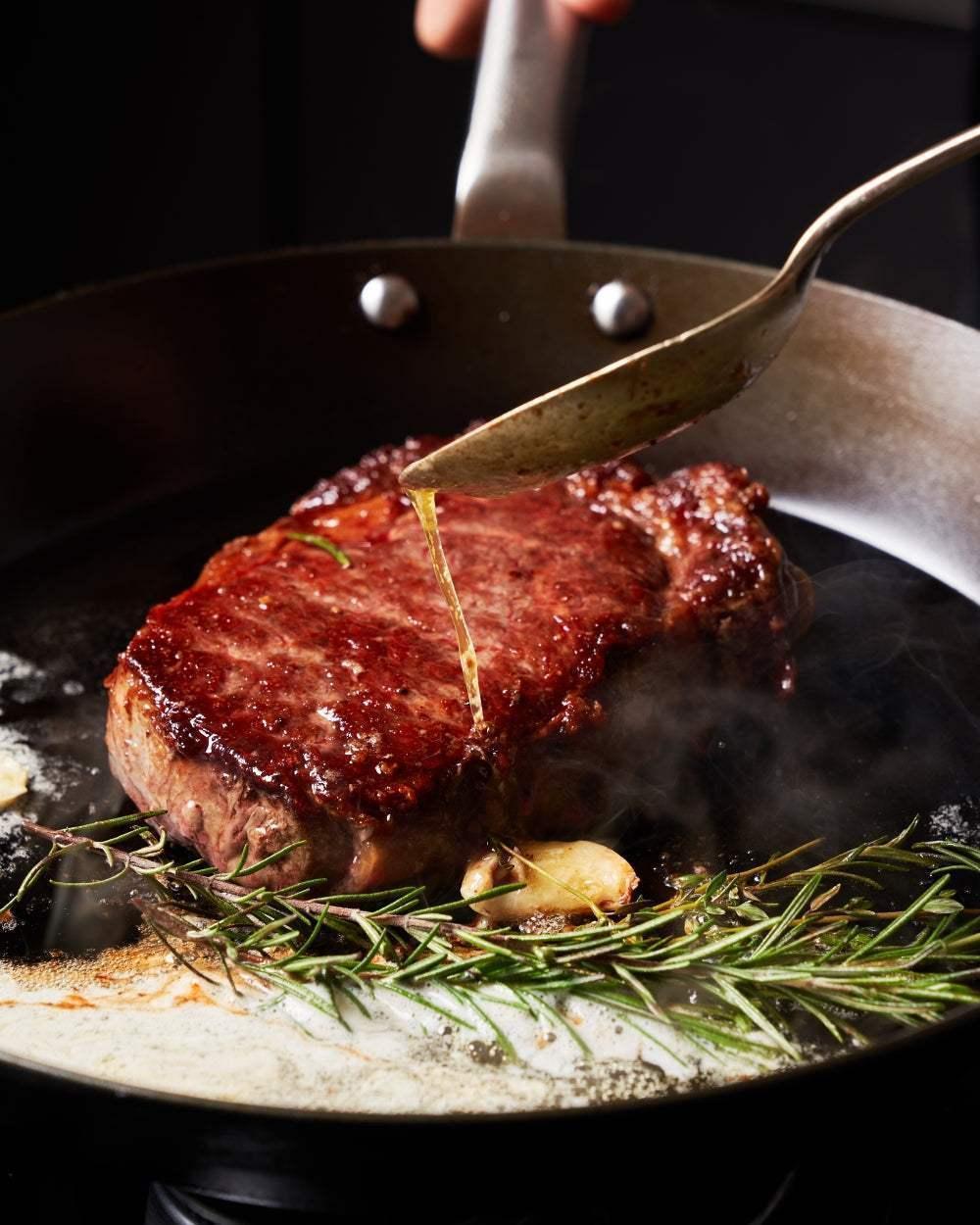 MAKO Black Steel Steak Pan - CookDineHost basting steak with butter herbs and garlic