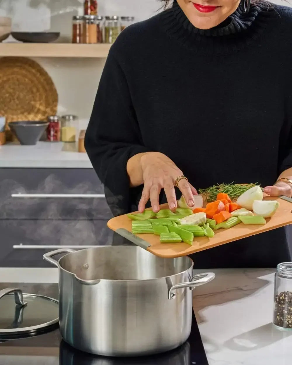 Woman adding fresh vegetables into stainless steel stock pot on kitchen stove