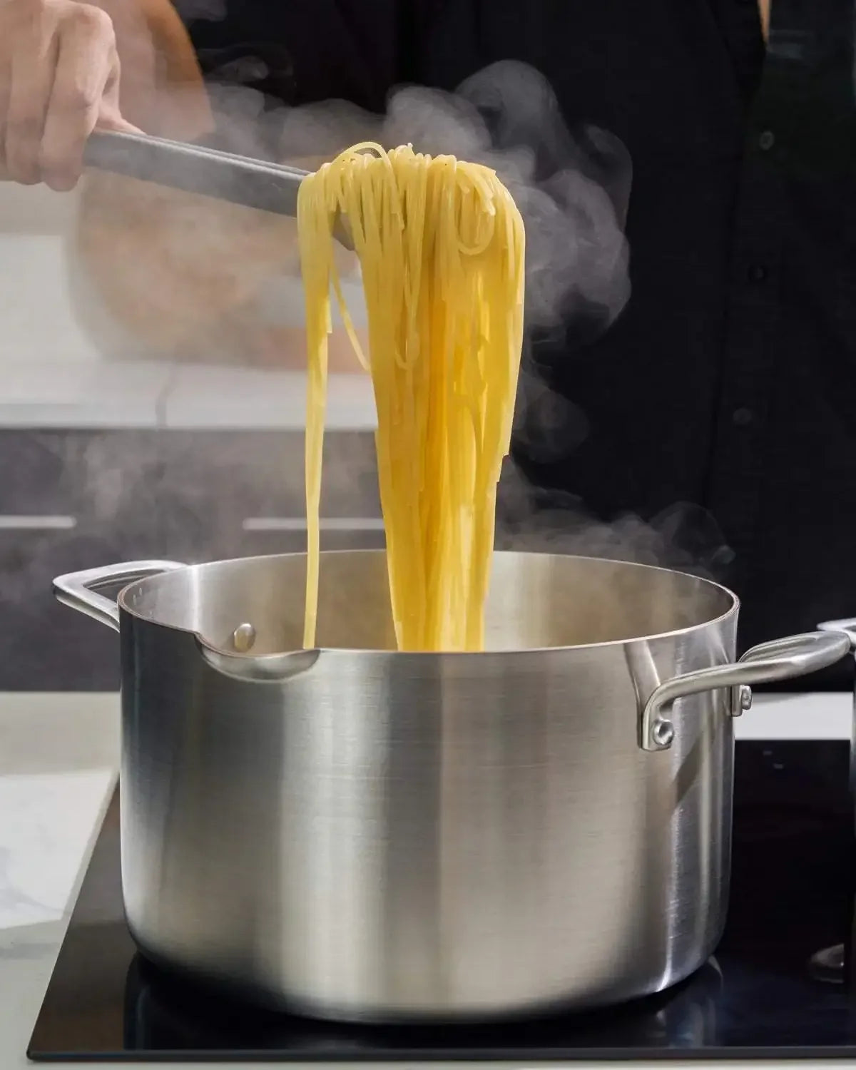 Stainless steel stock pot with handles on a stovetop, cooking steaming pasta