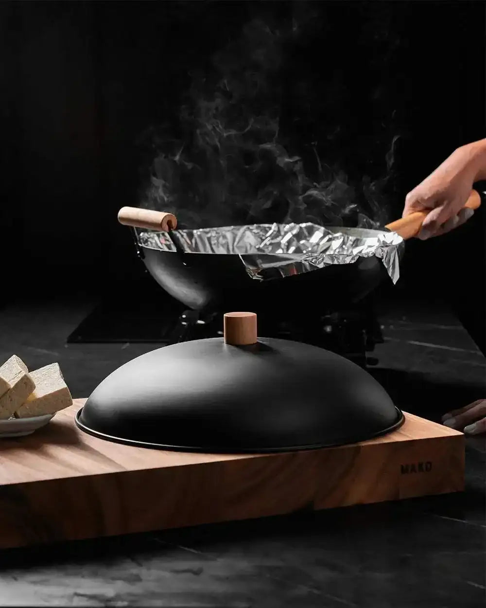 MAKO black steel wok and lid set by Marion Grasby on wood block, with tofu and steam rising