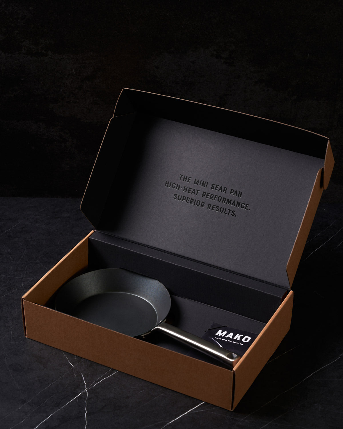 Black steel mini frying pan with stainless handle in a gift box on black marble surface