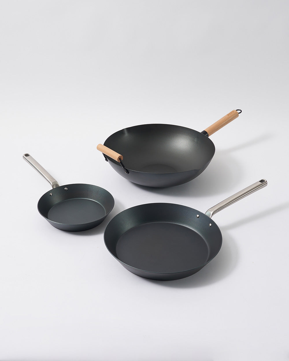 Three-piece black steel cookware set with wok, frying pan, and skillet on a white background.