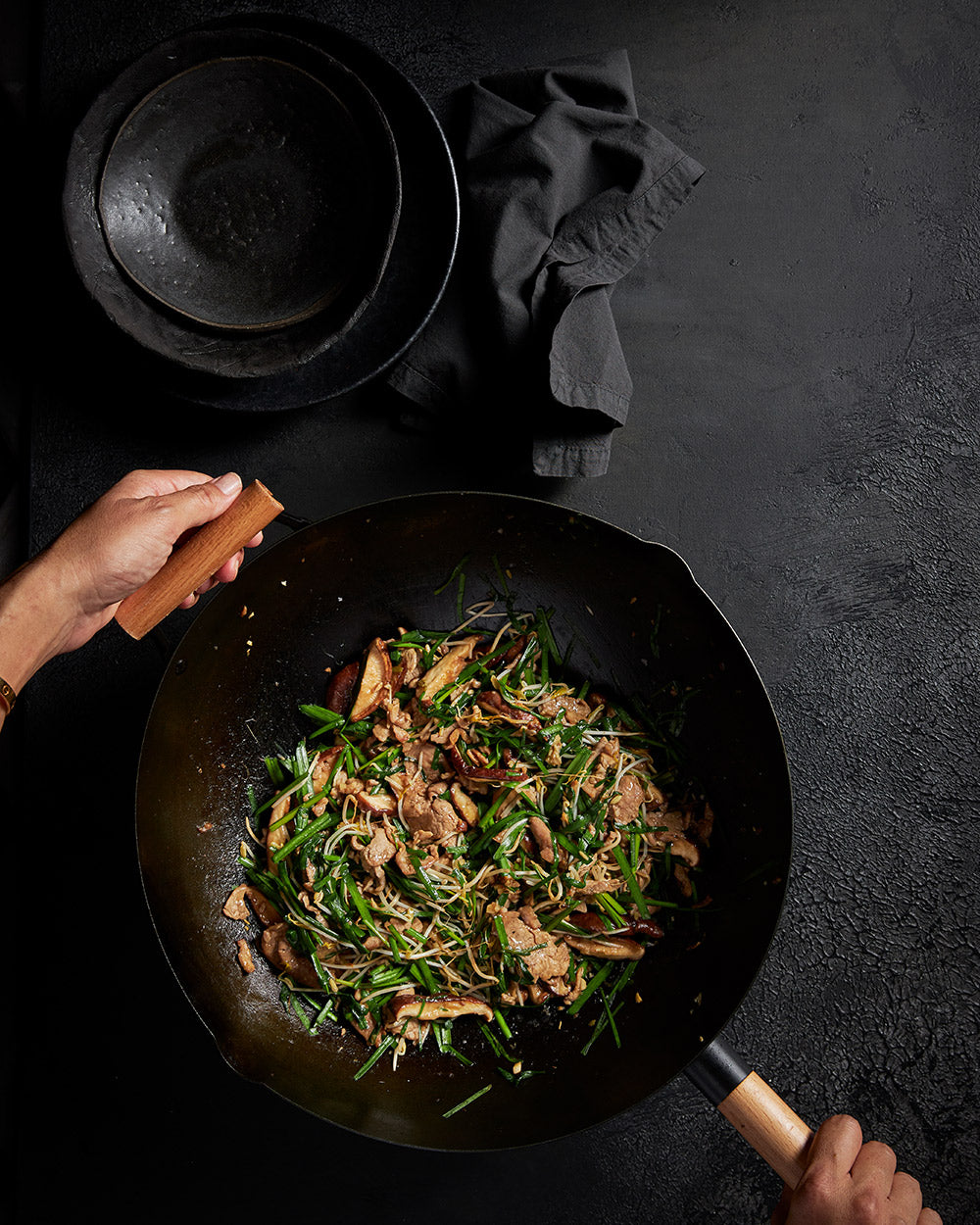 Stir fry vegetables and meat in a black wok with wooden handles on a dark background