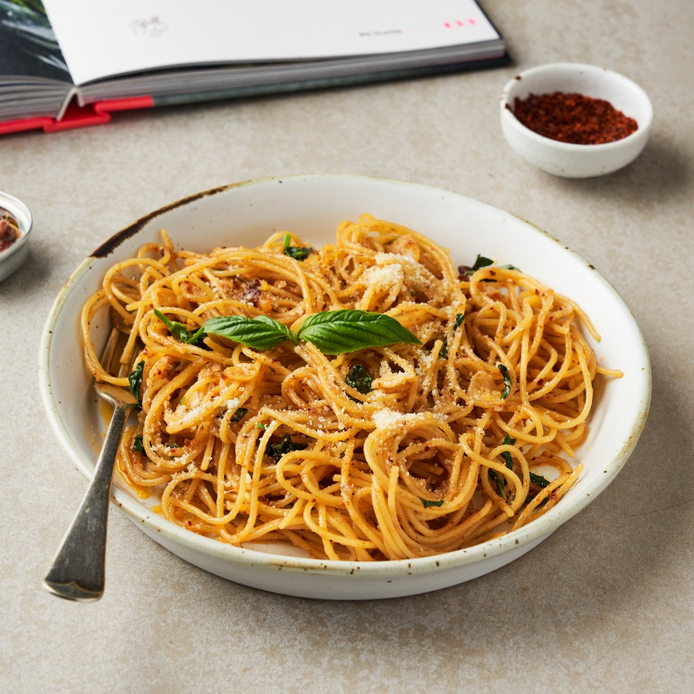 Spaghetti with tomato sauce, basil, and parmesan in a white bowl on a table, cookbook in background