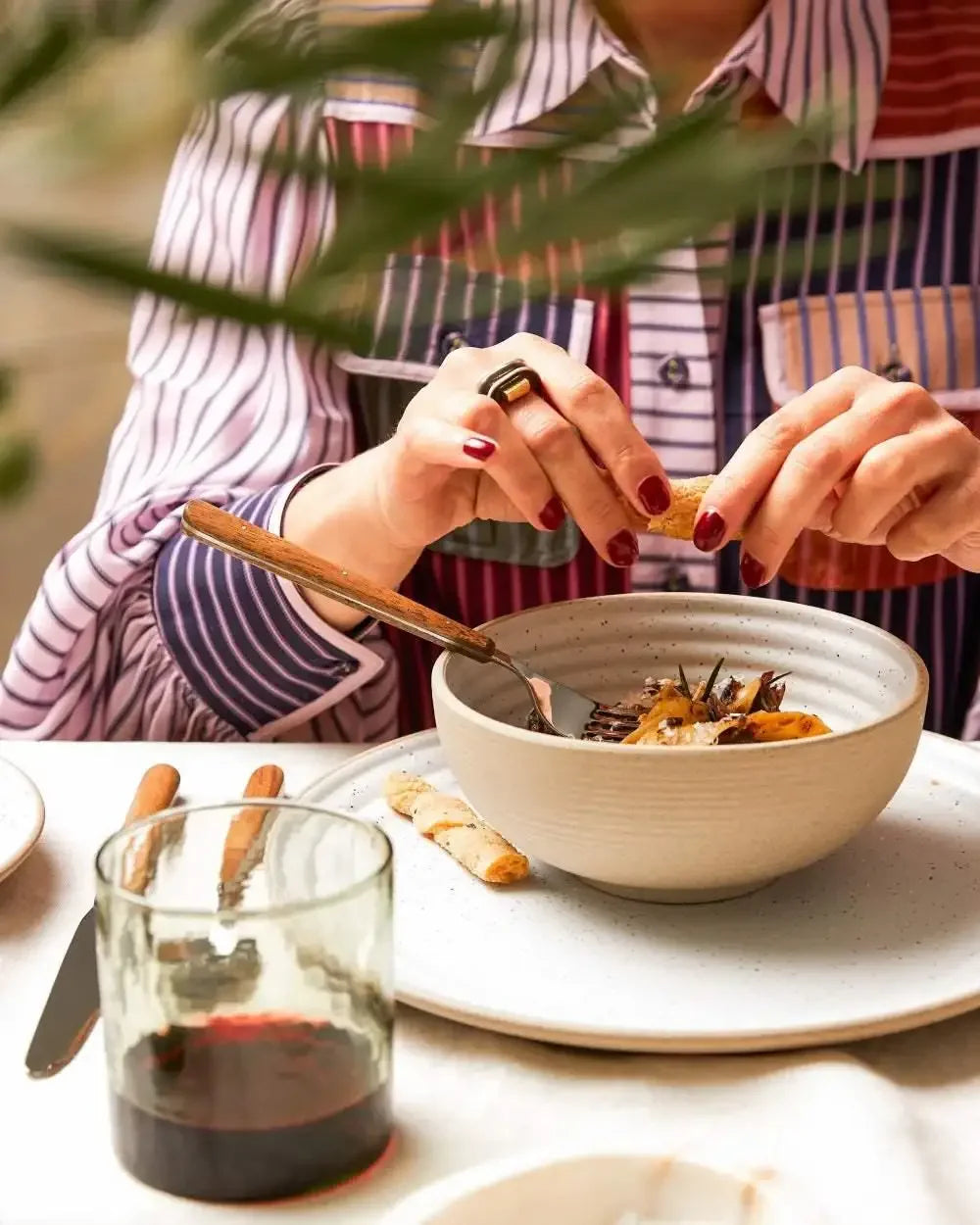 Modern stoneware cereal bowl with meal on a set table, person enjoying food, glass of red wine