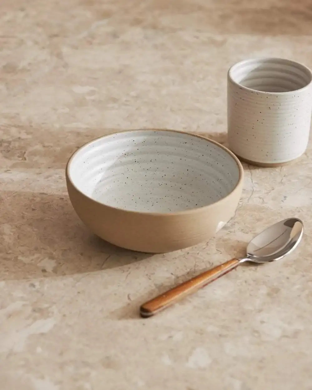 Asoke ceramic bowl and cup set with speckled glaze, wooden-handled spoon on marble surface by Marion Grasby