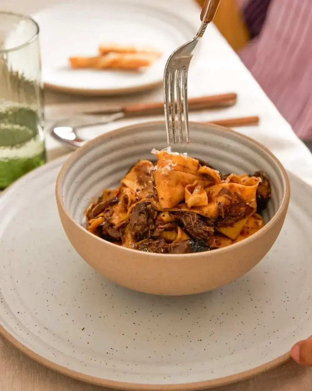Handmade ceramic cereal bowl with pasta dish, set on a speckled stoneware plate
