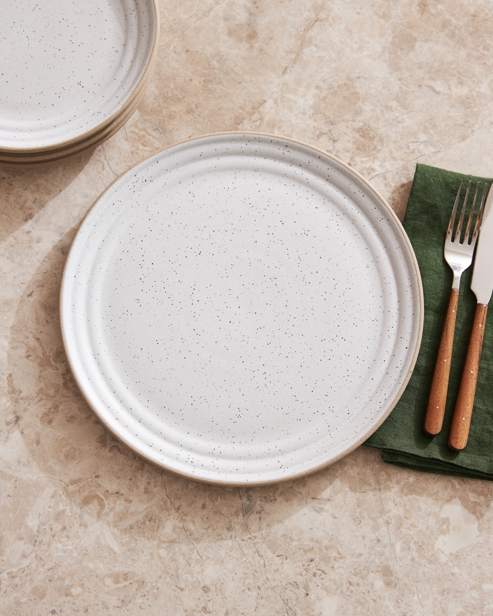 Set of speckled stoneware dinner plates with wooden-handled cutlery on marble surface