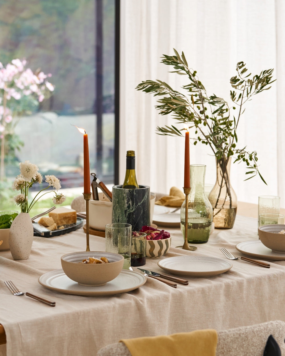 Neutral stoneware dinner plates and bowls set on an elegant, modern table with candles and flowers.
