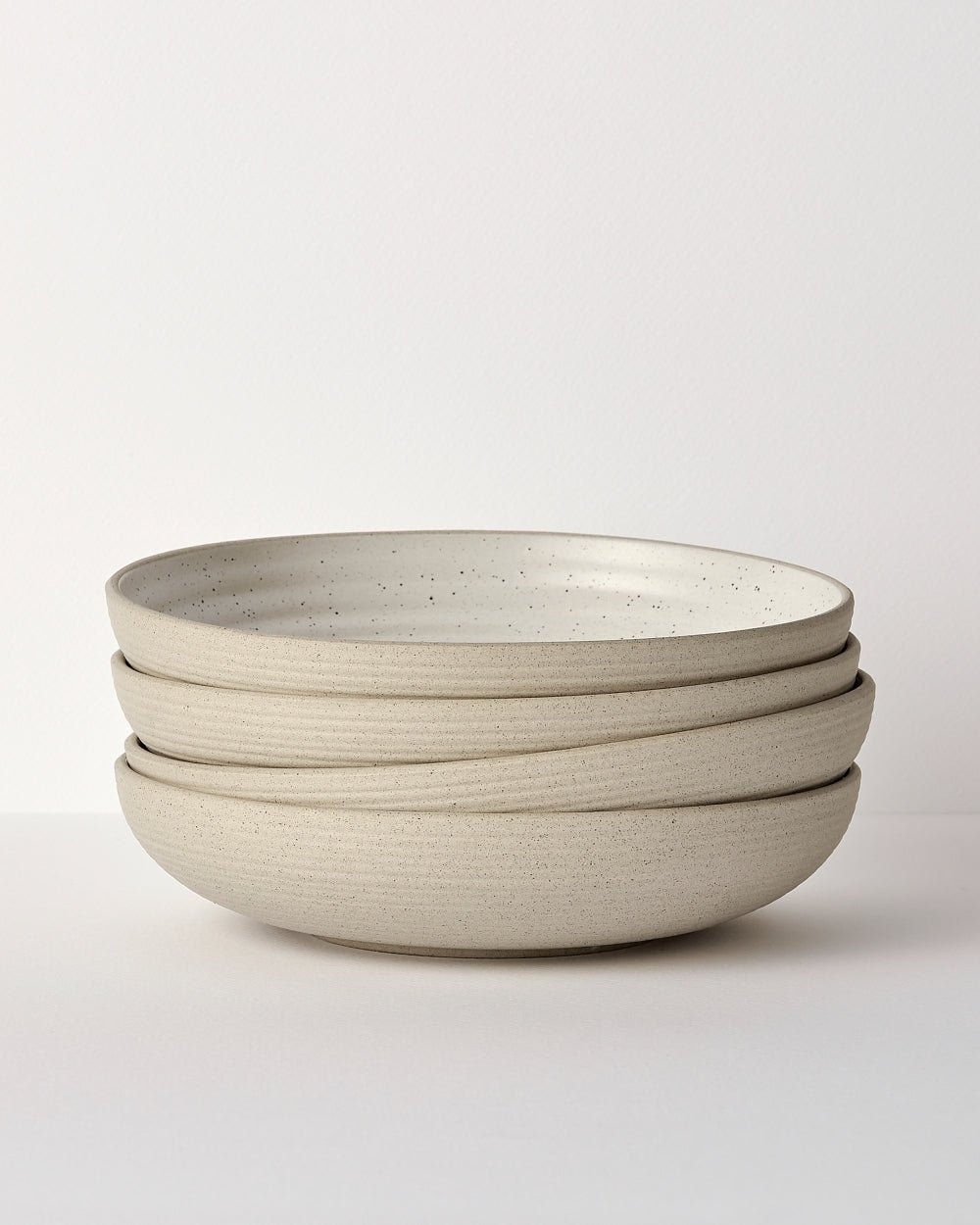Stack of four modern speckled stoneware dinner bowls on a white background