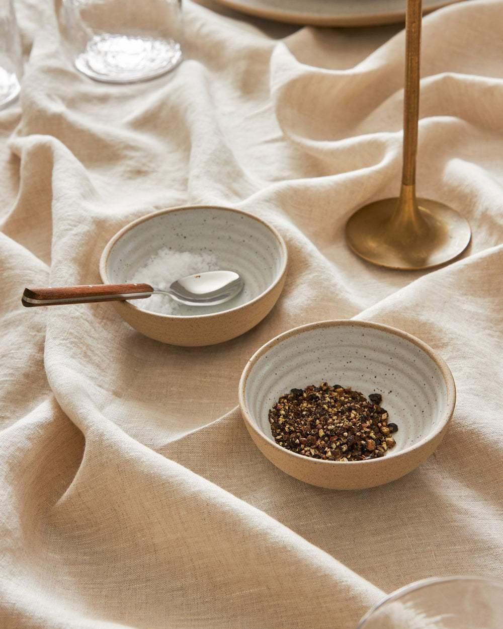 Asoke Mini Bowl and Spoon set by Marion Grasby with salt and pepper on a beige linen tablecloth