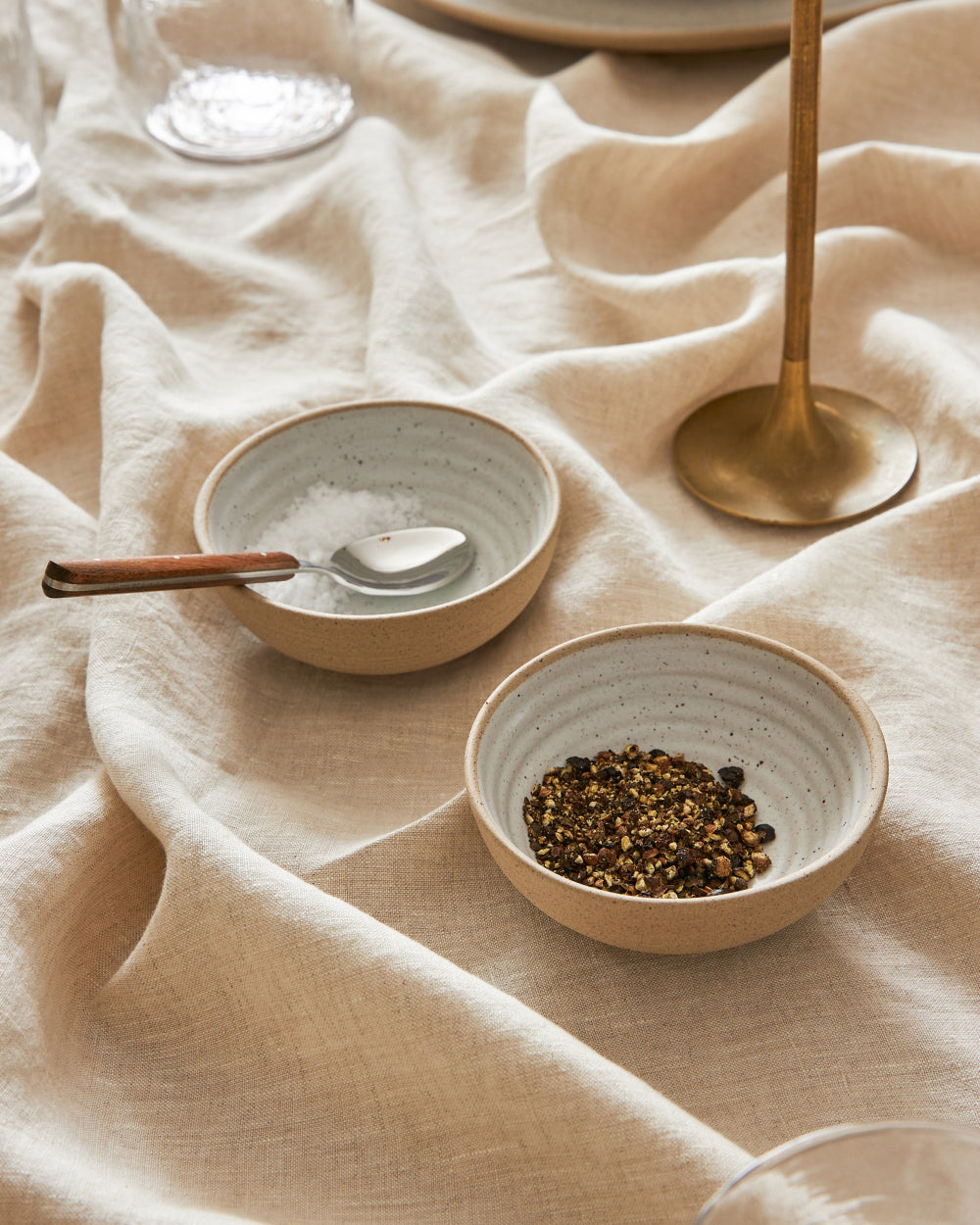 Ceramic mini bowl and spoon set on neutral tablecloth, filled with salt and spices