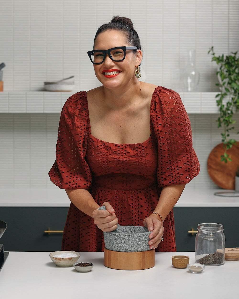 Woman using stone mortar and pestle in modern kitchen with spices on counter.
