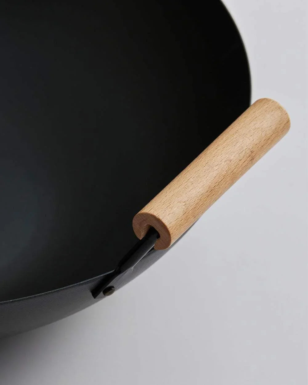 Close-up of black steel wok with smooth wooden handle on light background
