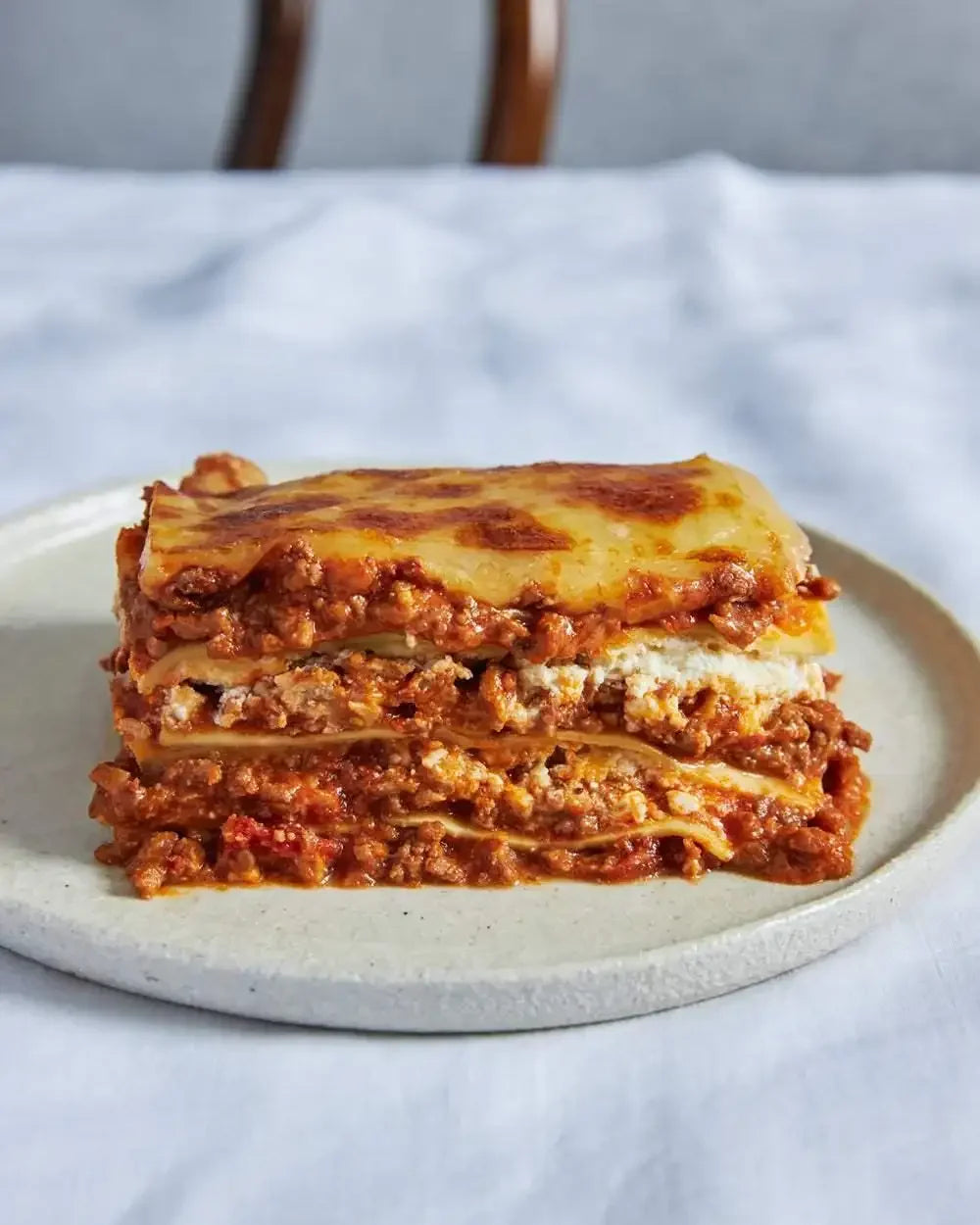 Close-up of a classic beef lasagna slice with cheese and tomato sauce on a ceramic plate