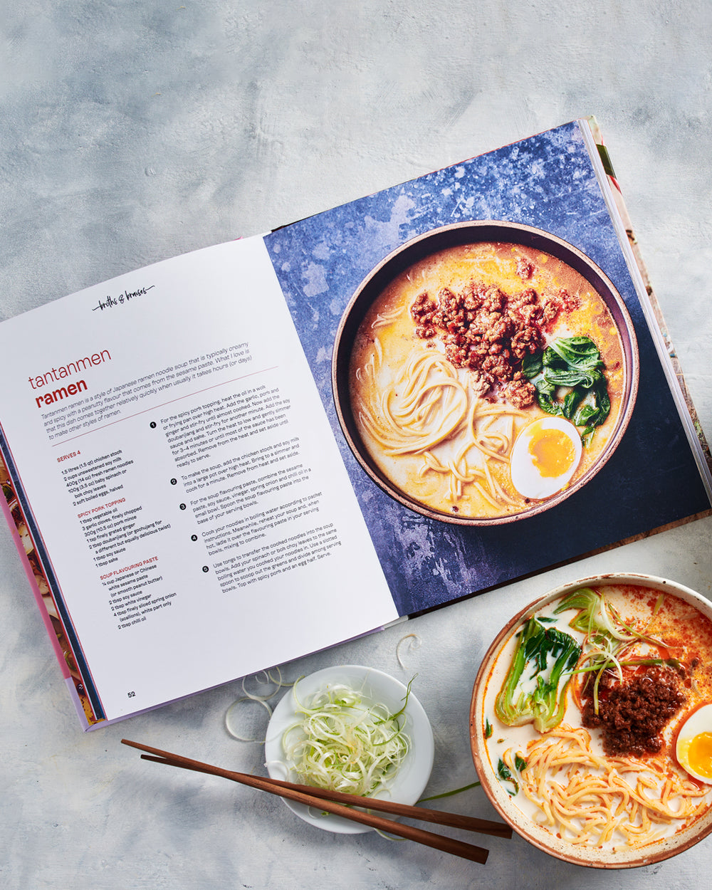 Open cookbook showing tantanmen ramen recipe with a bowl of ramen, chopsticks, and garnish