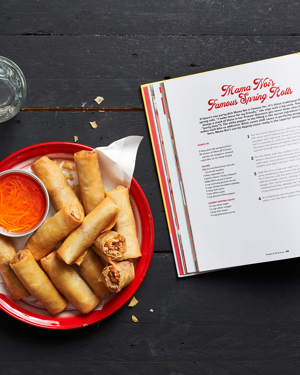 Plate of crispy spring rolls with dipping sauce next to open Asian cookbook on a dark table.