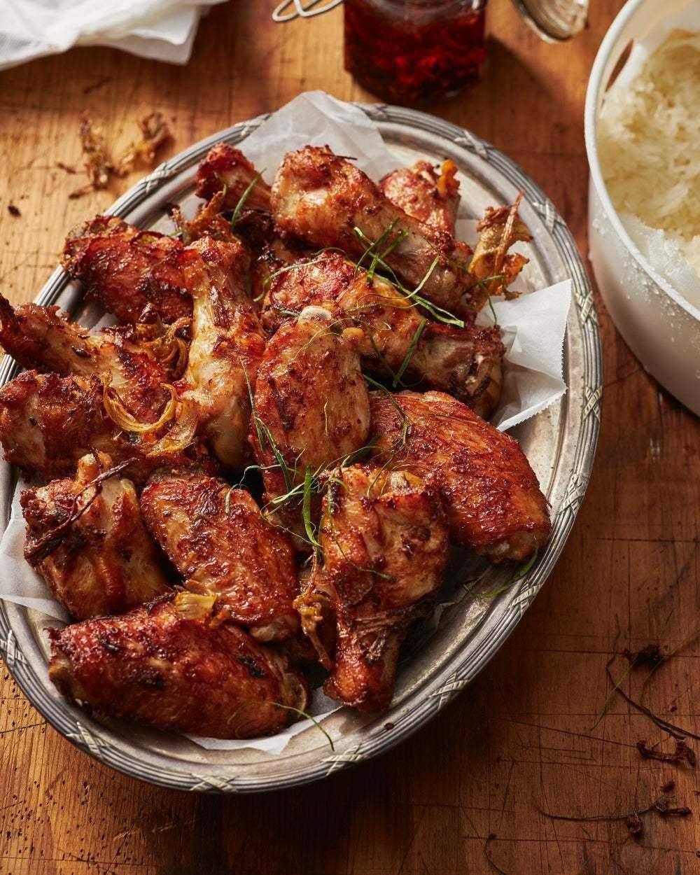 Platter of crispy Asian-style fried chicken wings on parchment, with white rice and herbs