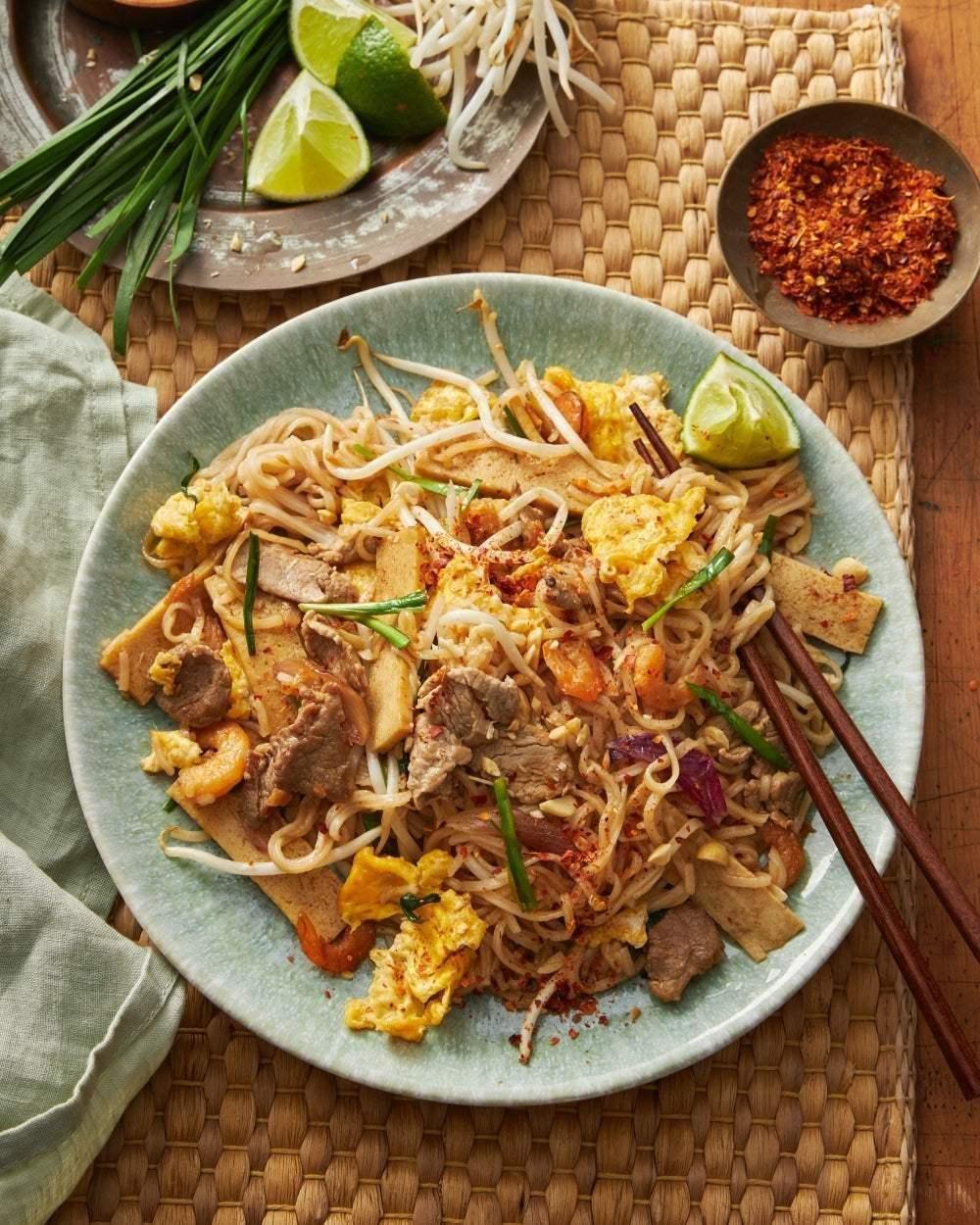Plate of Asian stir-fried noodles with beef, egg, tofu, bean sprouts and lime wedges