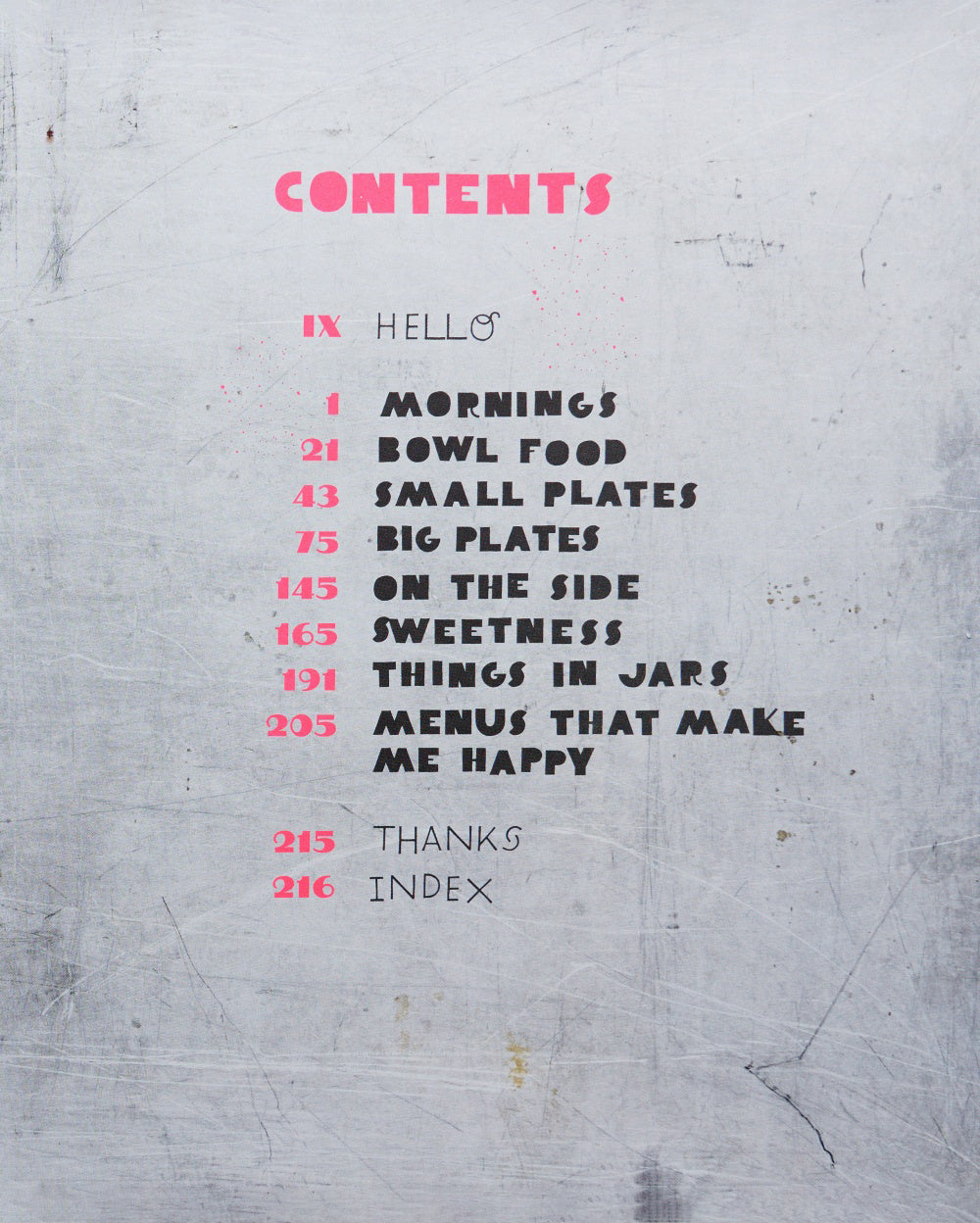 Cookbook contents page with pink and black text, listing recipe sections like mornings, bowl food, small plates, and big plates on a textured gray background.