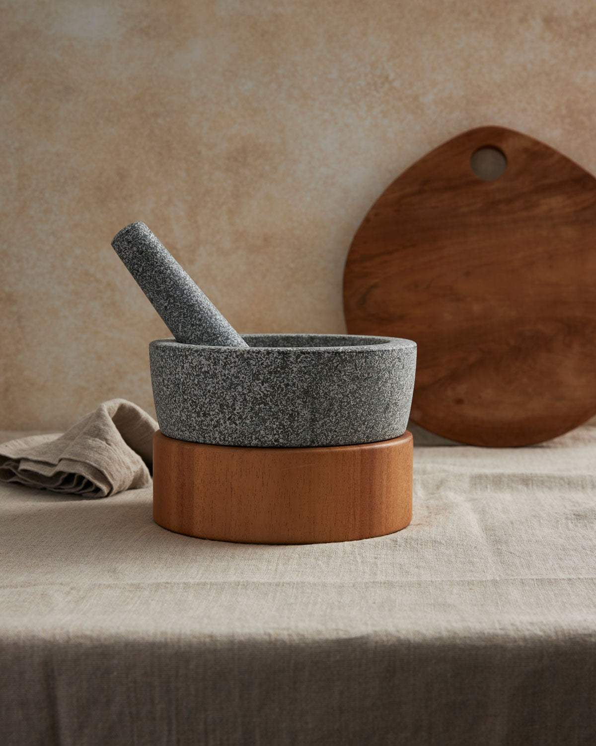 Granite mortar and pestle with wooden base on linen tablecloth, kitchen setting