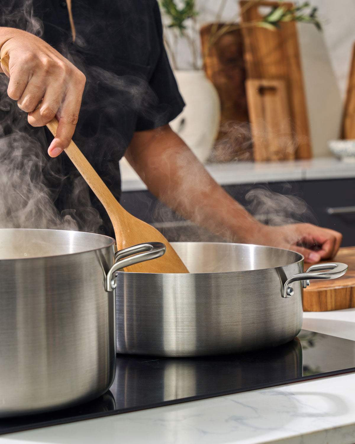 Cooking with stainless steel pots on a stovetop, steam rising, wooden spoon stirring