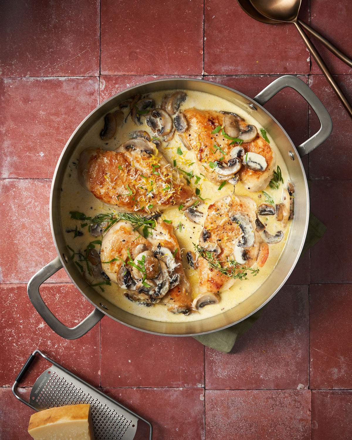 Creamy chicken and mushrooms in skillet with fresh herbs on red tile background